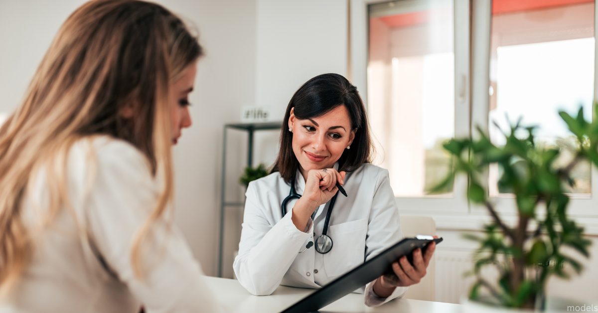 A female doctor holding clipboard while looking at other woman (models)