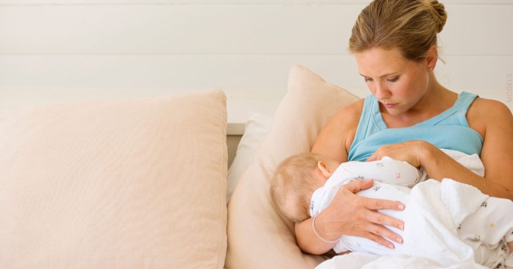 Woman laying in bed breastfeeding her baby (models)