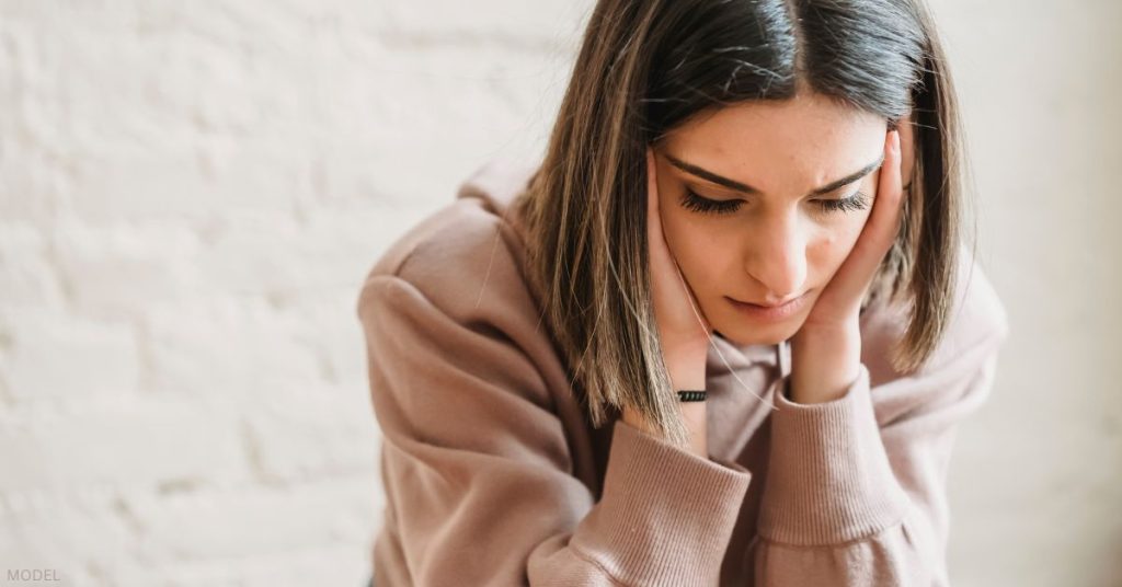 Woman looking concerned with her head in her hands looking down (model)