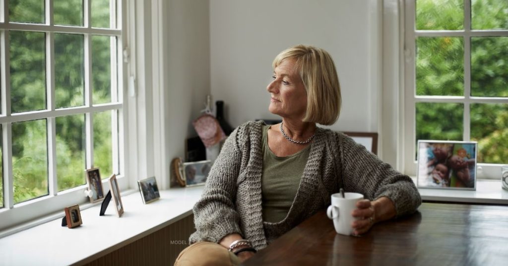 female (model) stares off into distance from her dining room table